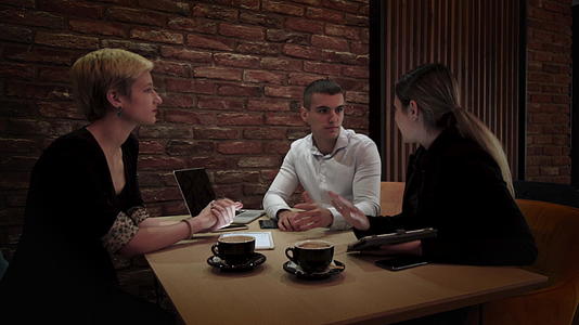 深夜在一家现代咖啡馆开会下班后三位年轻的商业同事视频的预览图
