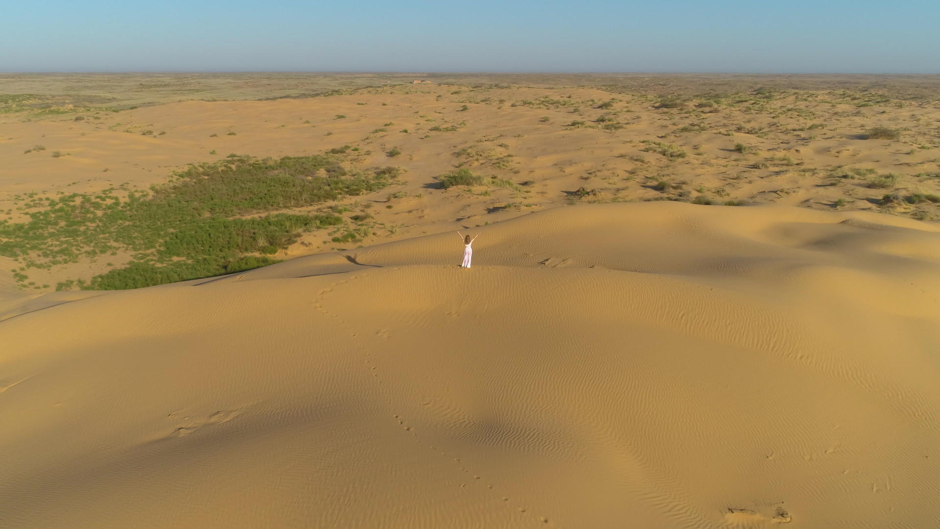 一个穿着白色裙子和长发的孤独的年轻女子在沙漠的海滩上举起手视频的预览图