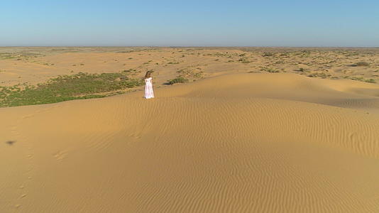 孤独的年轻女子留着白色的裙子和长发仍然停留在沙漠的海滩上视频的预览图