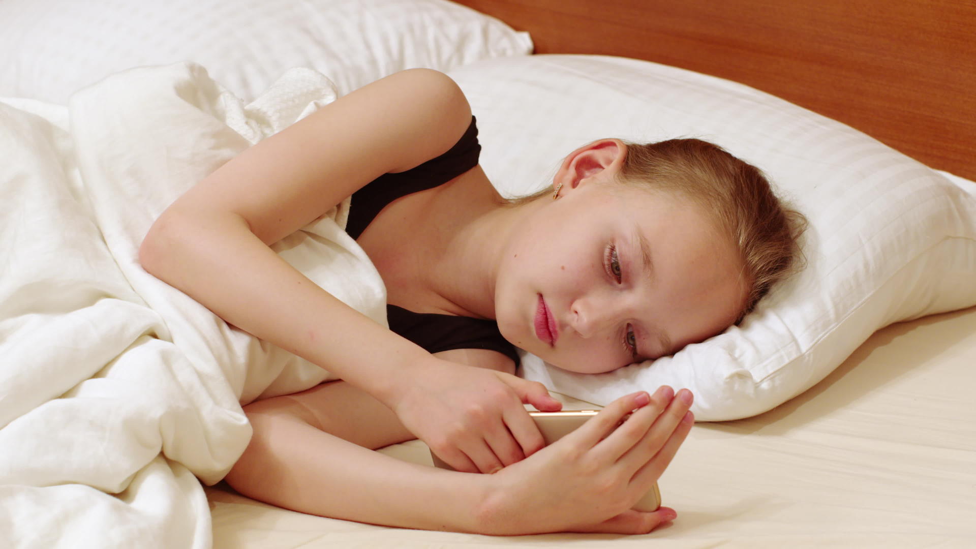 年轻女子看着手机躺在白色的床上十几岁的女孩躺在白色的卧室里视频的预览图