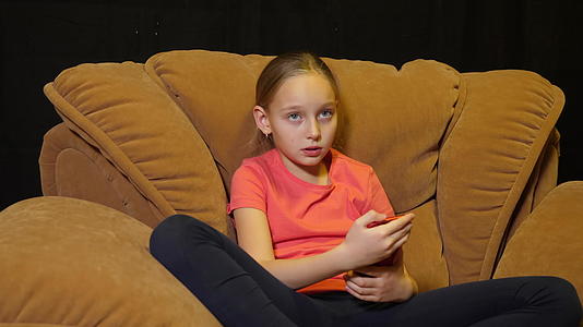 坐在舒适椅子上的女孩用手机在黑色背景下使用手机视频的预览图