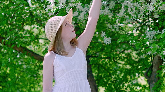 夏天果园里戴着草帽的年轻女孩闻着苹果树的花朵视频的预览图