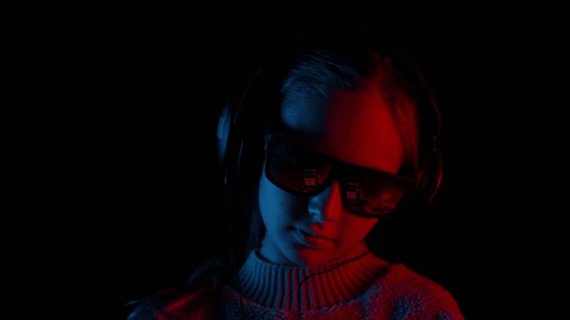 戴着耳机的年轻女孩在黑暗的工作室里使用红色和蓝色的灯光视频的预览图