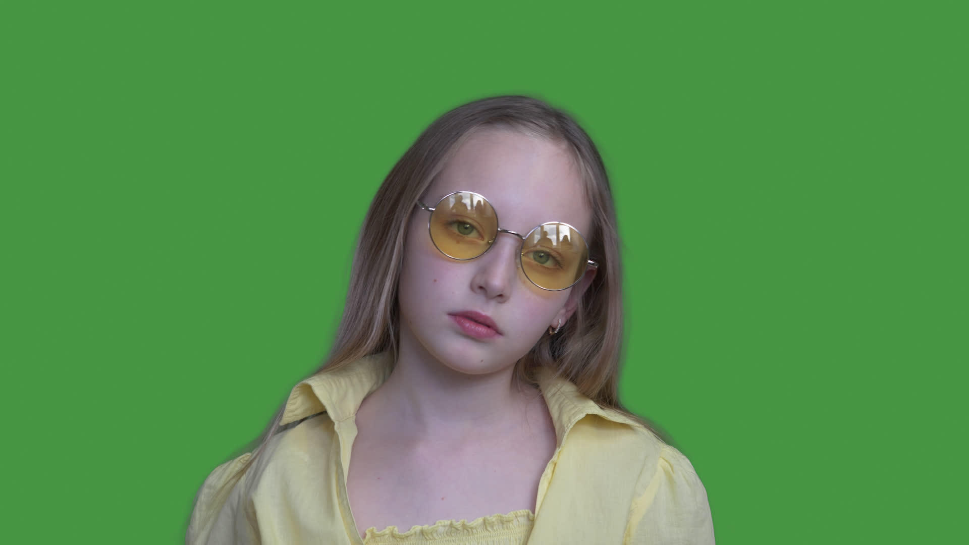 严肃的年轻女孩戴着黄色眼镜和绿色背景的相机视频的预览图