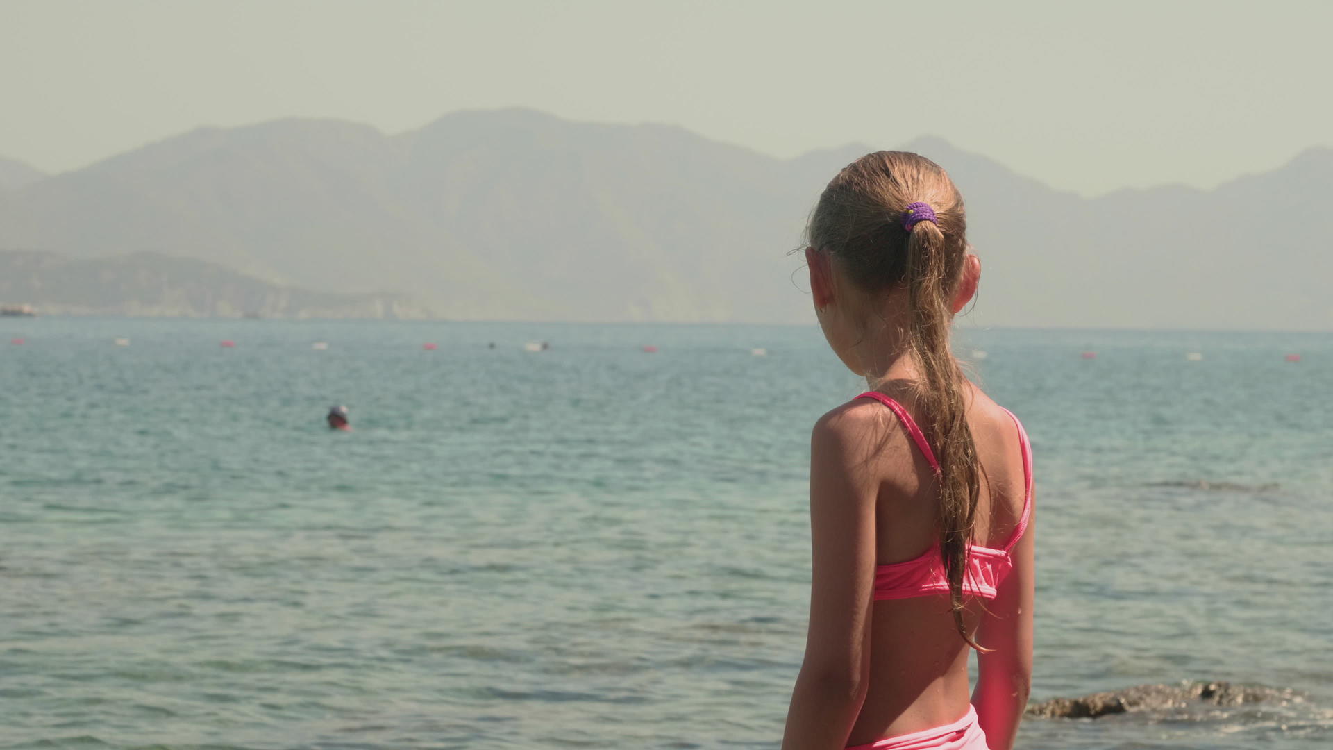 穿着粉色泳衣的年轻女孩在阳光明媚的海滩上欣赏海景视频的预览图