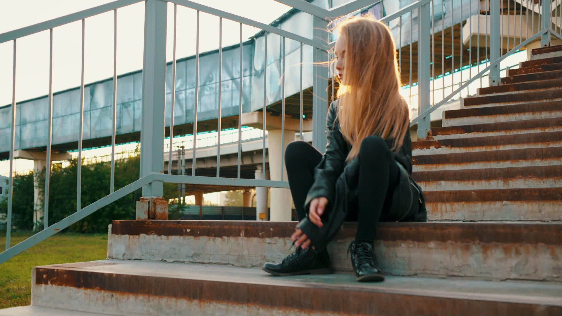 一个穿着黑色皮夹克的年轻女孩坐在楼梯上的时尚模特视频的预览图