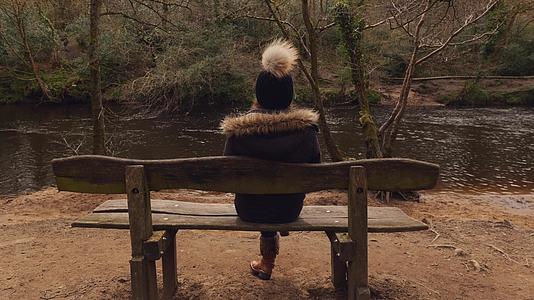 坐在树林里的河边的年轻女人视频的预览图