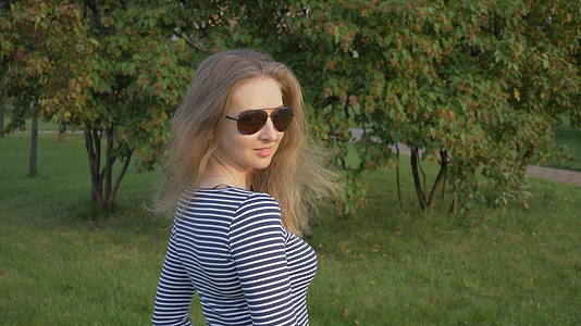 穿着条纹衬衫和太阳镜的年轻美女转身把长发扔进了绿色公园视频的预览图