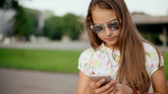 在户外手机上玩游戏的笑女孩视频的预览图