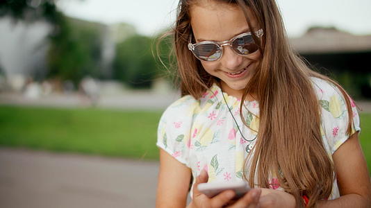 夏天在公园里微笑的女孩正在用手机上网视频的预览图