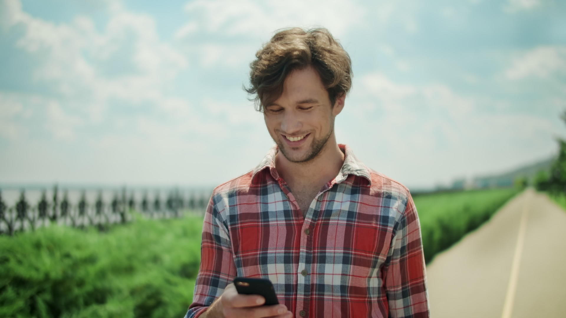 快乐的男人在外面使用智能手机走在公园路上笑的人视频的预览图