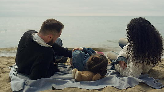 父母的孩子躺在海边大自然的沙滩上视频的预览图