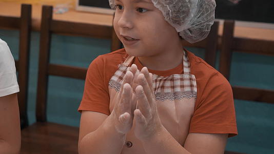 小男孩在烹饪课上滚面团前用面粉搓手小男孩的厨师在学校视频的预览图
