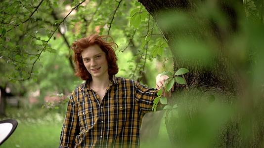红发小男孩站在树旁的花园里视频的预览图