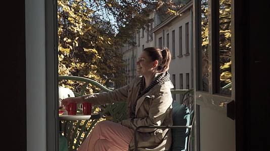 年轻的白人女性在阳光明媚的秋天坐在露天阳台上享受茶叶视频的预览图