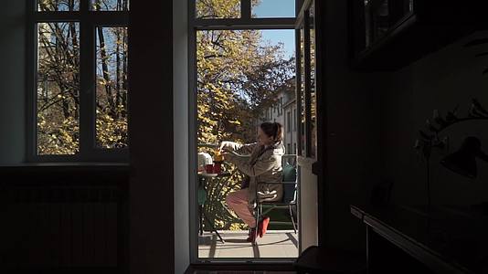 白种年轻女子将茶倒入露天阳台的杯子中视频的预览图