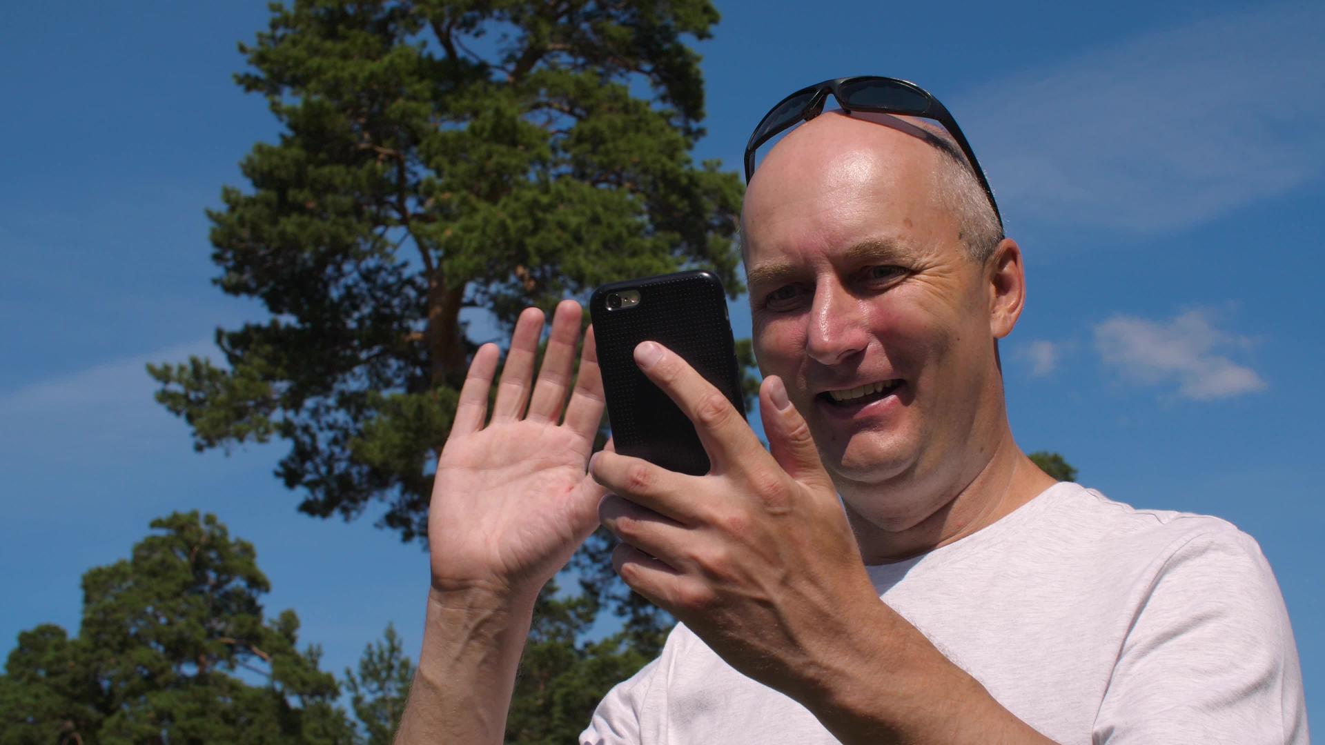 夏天在公园里用手机聊天时微笑的男人视频的预览图