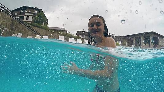 下雨时游泳池里快乐的青少年微笑着看着相机视频的预览图