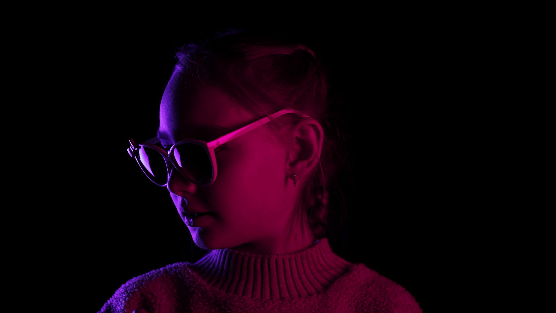 在霓虹灯照明的黑暗工作室里戴着墨镜的微笑女孩看着相机视频的预览图