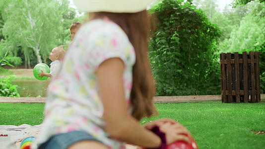 两兄弟在公园里玩球可爱的姐姐坐在户外毯子上视频的预览图