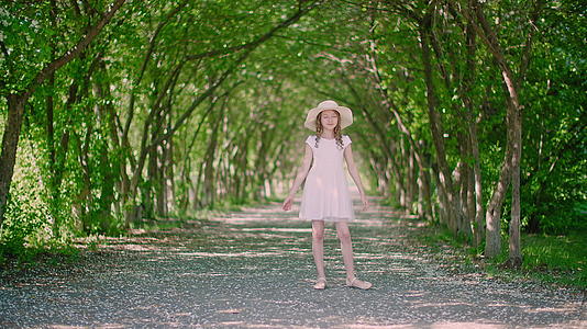 快乐的卷发女孩穿着白色连衣裙戴着帽子在春天的公园里开花视频的预览图