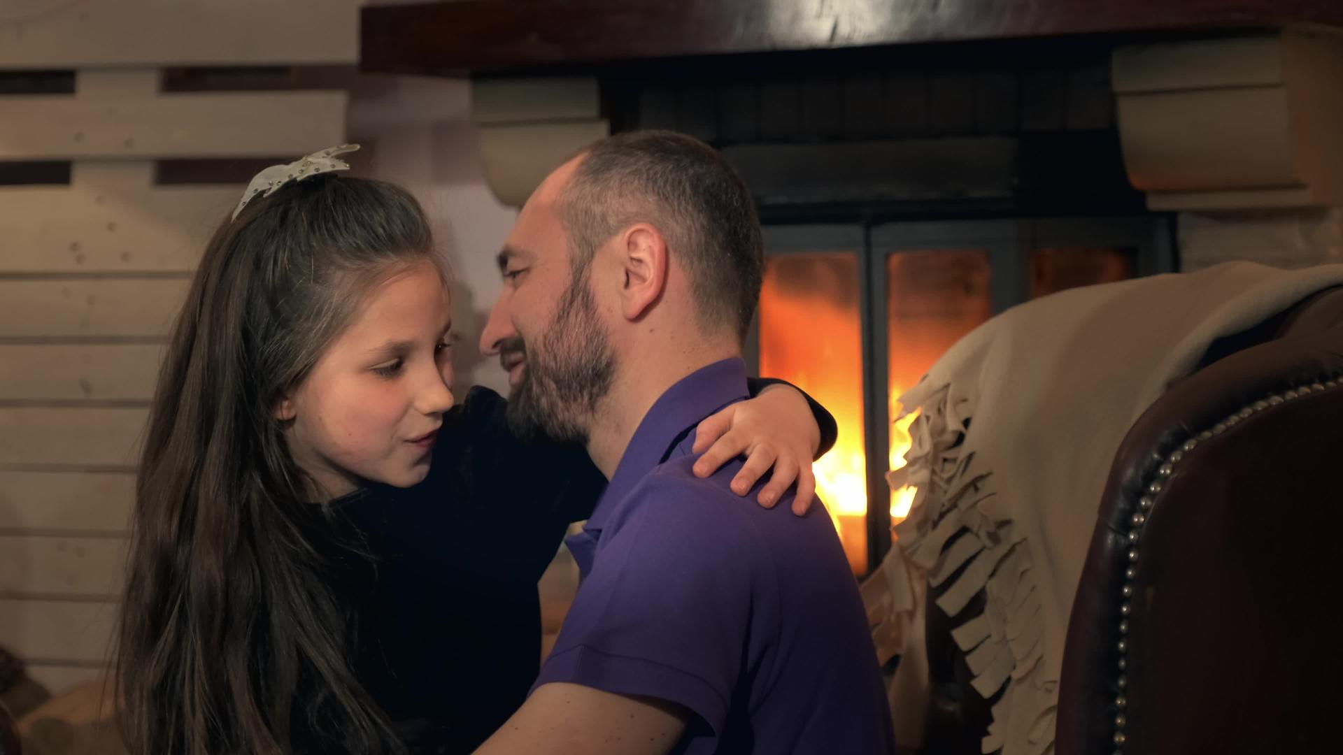 快乐的父亲和小女儿拥抱着对方坐在壁炉旁的椅子上视频的预览图