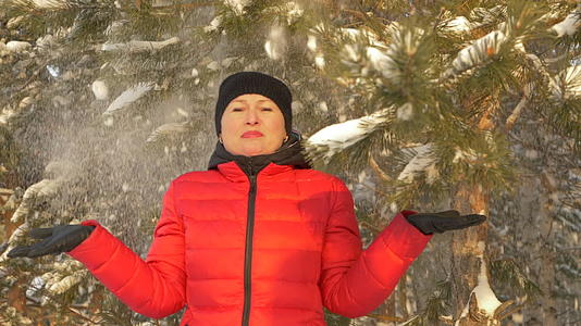 快乐的女士站在雪花下在冬天的森林里从雪树下慢慢地移动视频的预览图