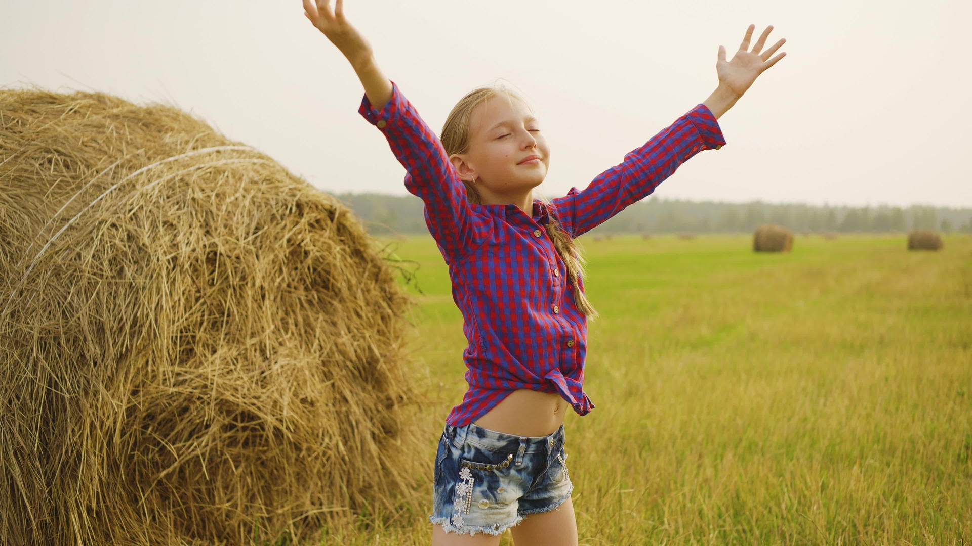 快乐的女孩在干草堆的背景下向天空伸出手女孩在农村收获视频的预览图