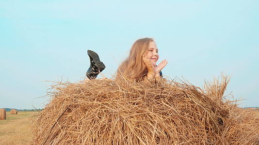 快乐的女孩躺在收割场的干草堆上快乐的女孩在农村的田野里视频的预览图