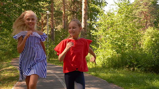 欢笑的女友在人行道上奔跑在夏天阳光明媚的公园里视频的预览图