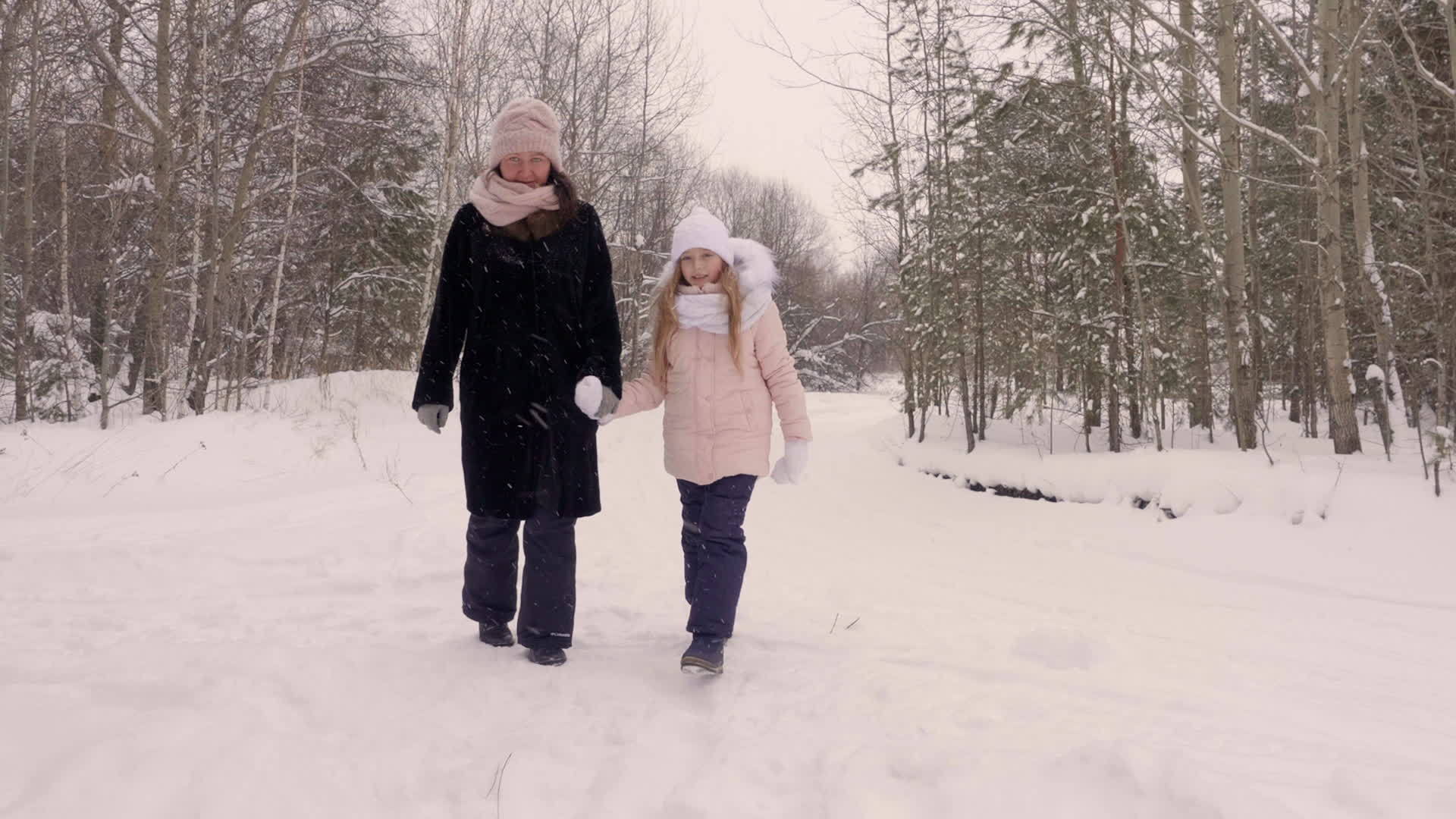 母亲和女儿一起走过了冬天的森林之路松树下的雪松树视频的预览图