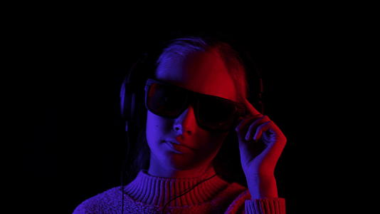 快乐的女孩在耳机里黑色的太阳镜在红色和蓝色的灯光下视频的预览图