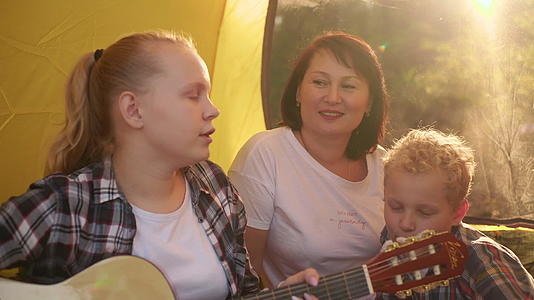 有两个孩子坐在帐篷里受吉他和两个孩子的幸福家庭视频的预览图