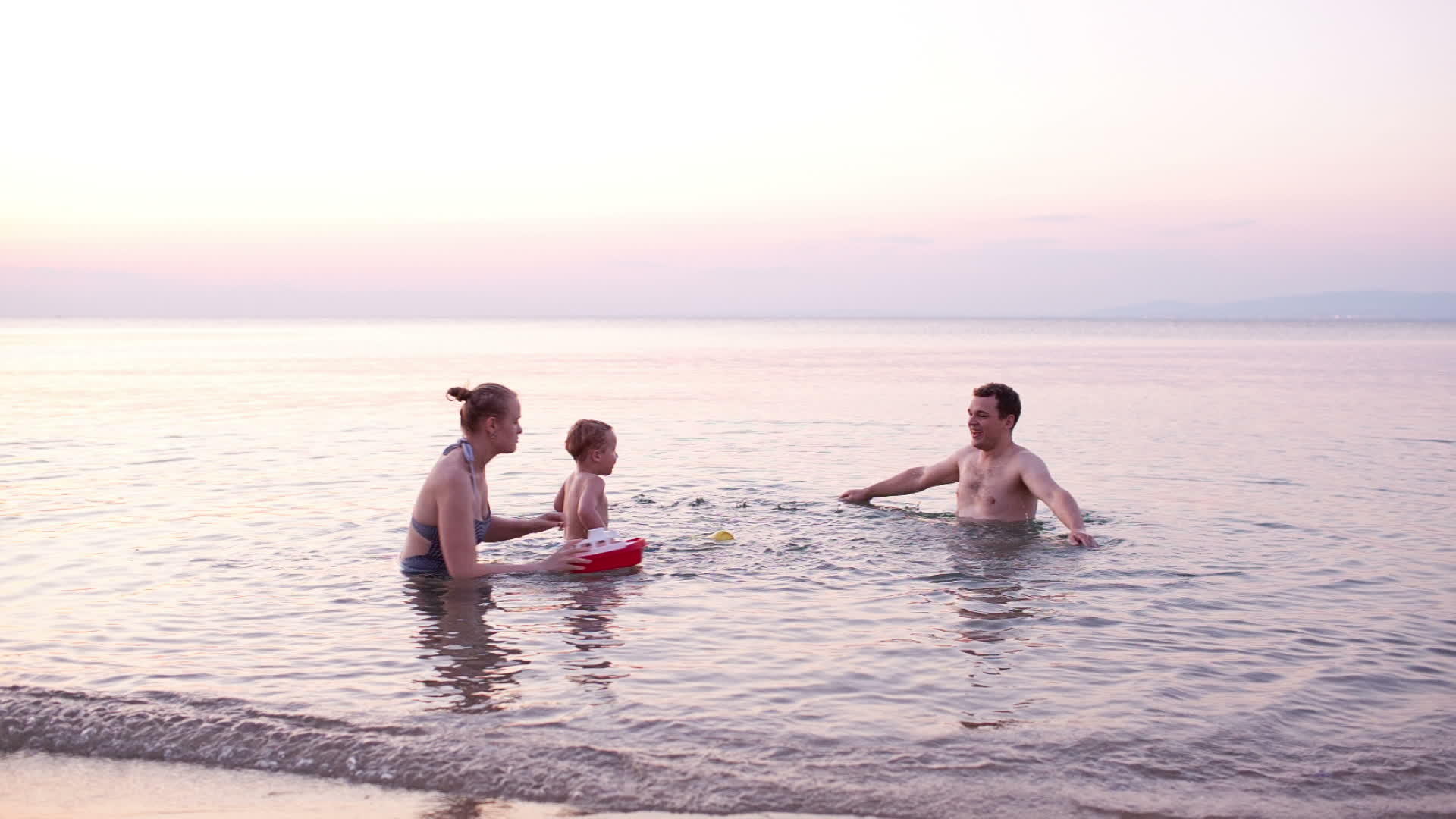 年轻家庭在日落时玩红色玩具船视频的预览图