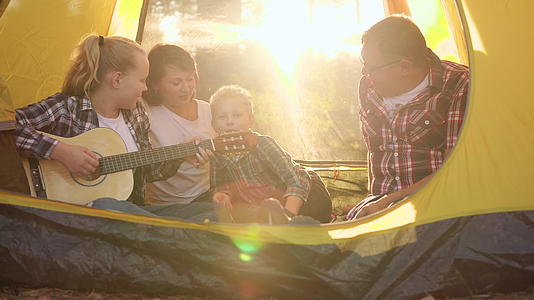 幸福的家庭在阳光下的露营帐篷里用吉他唱歌视频的预览图