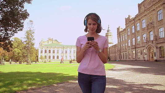 使用耳机的快乐女性在校园区域行走视频的预览图