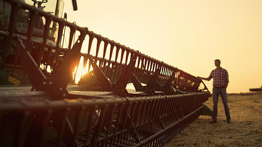 剪影农民站在田间观察联合收割机收获黄金夕阳视频的预览图