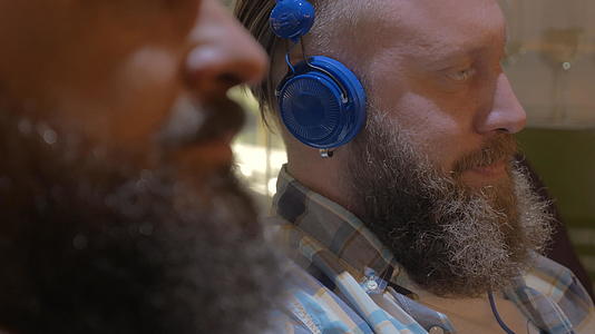 两个留胡子的男人用五颜六色的耳机听音乐视频的预览图
