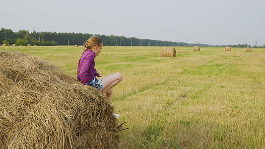 快乐的女孩在农田的干草堆上微笑女孩在农村的田野里站起来视频的预览图