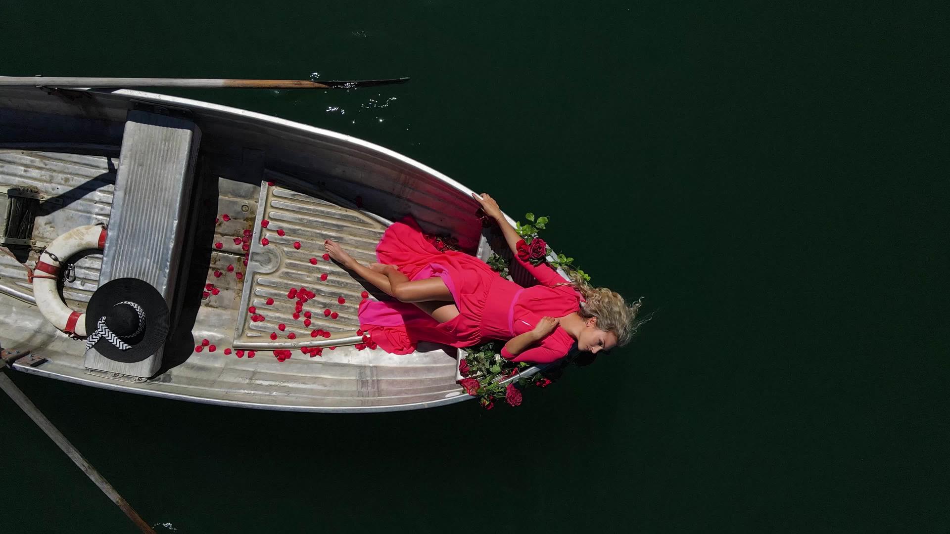 一个穿着红色裙子的漂亮女人留着长长的金发在瑞士山湖上坐船视频的预览图