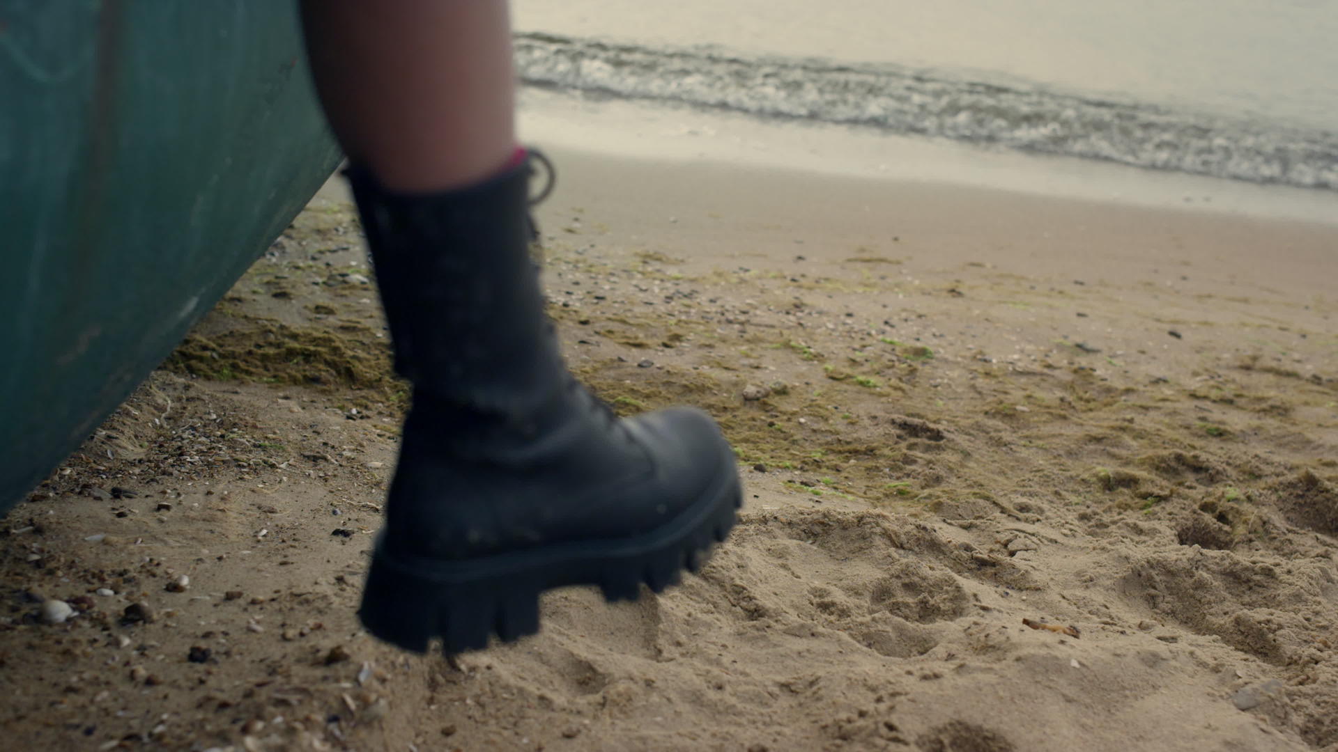 女人穿着黑色靴子腿挂在老船上站在沙滩上视频的预览图