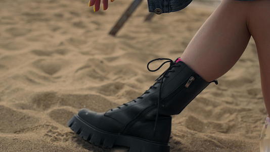 女孩穿着黑色靴子双腿躺在海滩上视频的预览图
