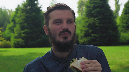 一个年轻人在公园里吃三明沙拉视频的预览图