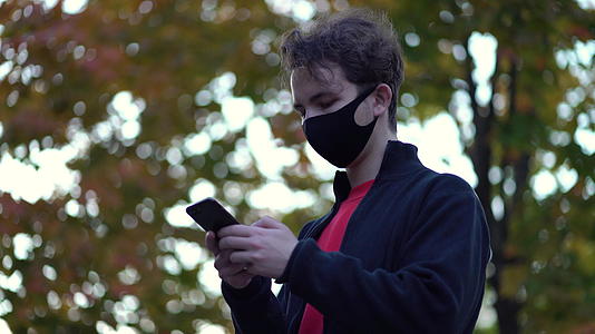 一个戴着防护医用面具的肖像男孩走上街头用手机短信卷轴视频的预览图