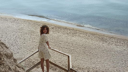 优雅的女士站在楼梯平台上观看美丽的沙滩视频的预览图