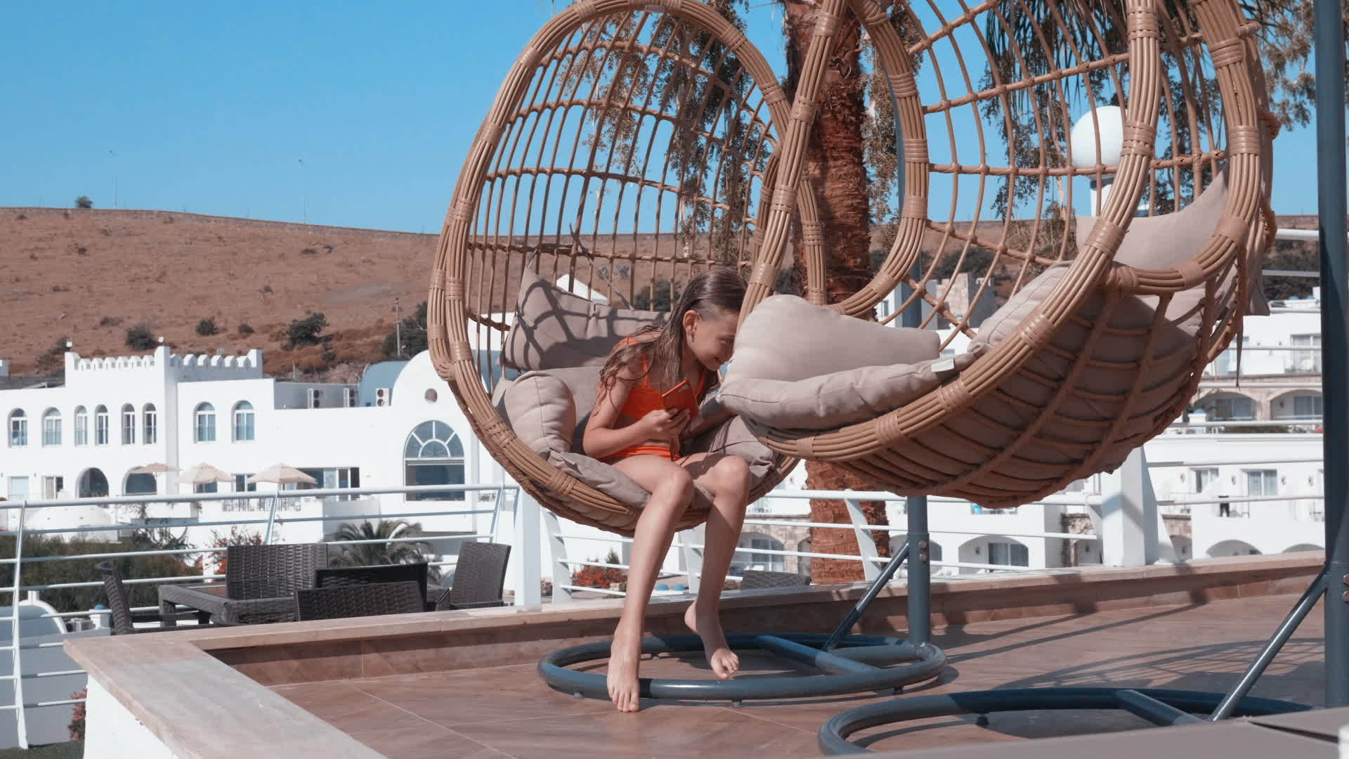 快乐的女孩在度假酒店的吊椅上用手机放松阳光明媚阳光明媚视频的预览图