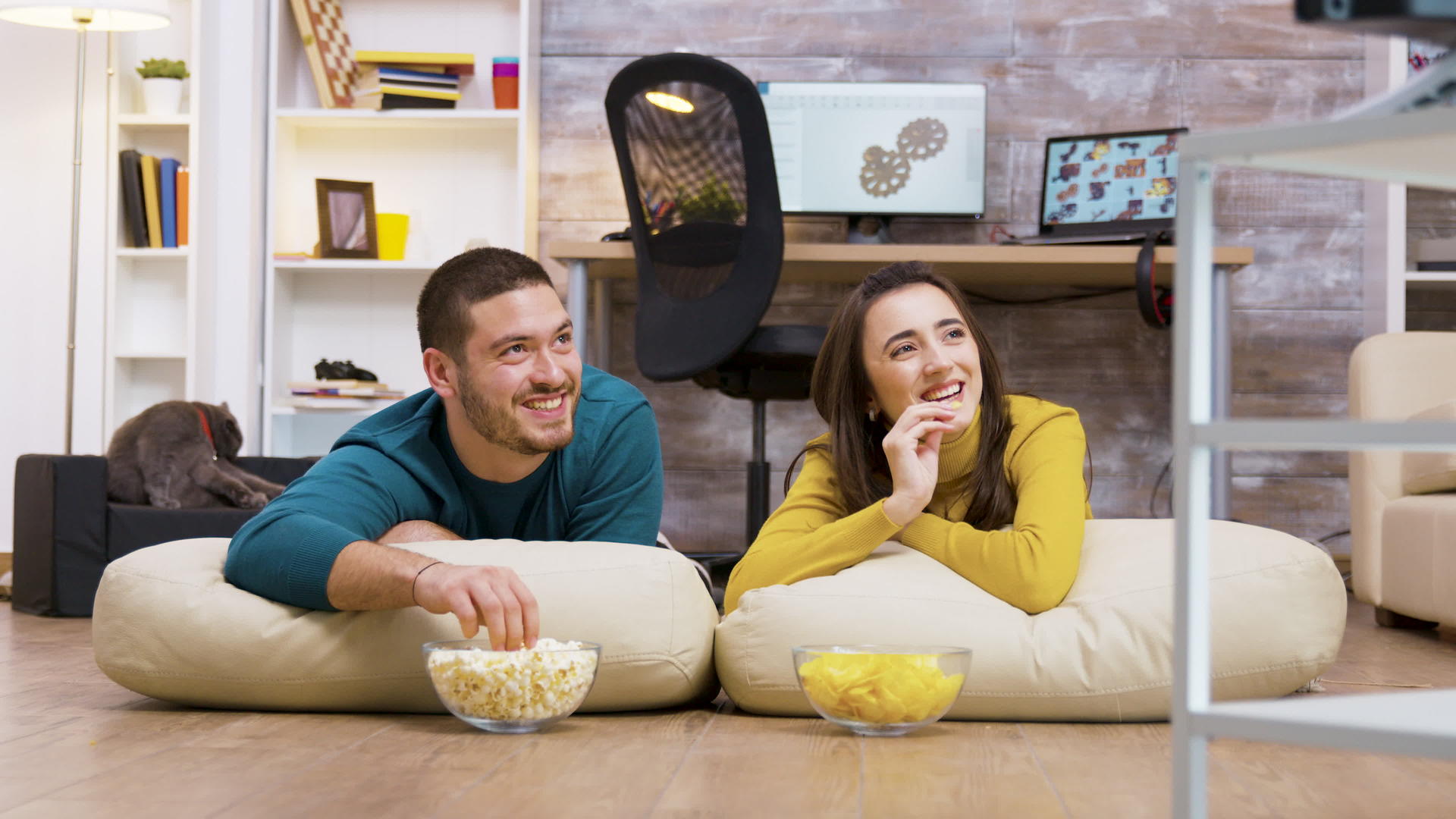 一对快乐的夫妇看着电视坐在枕头上视频的预览图