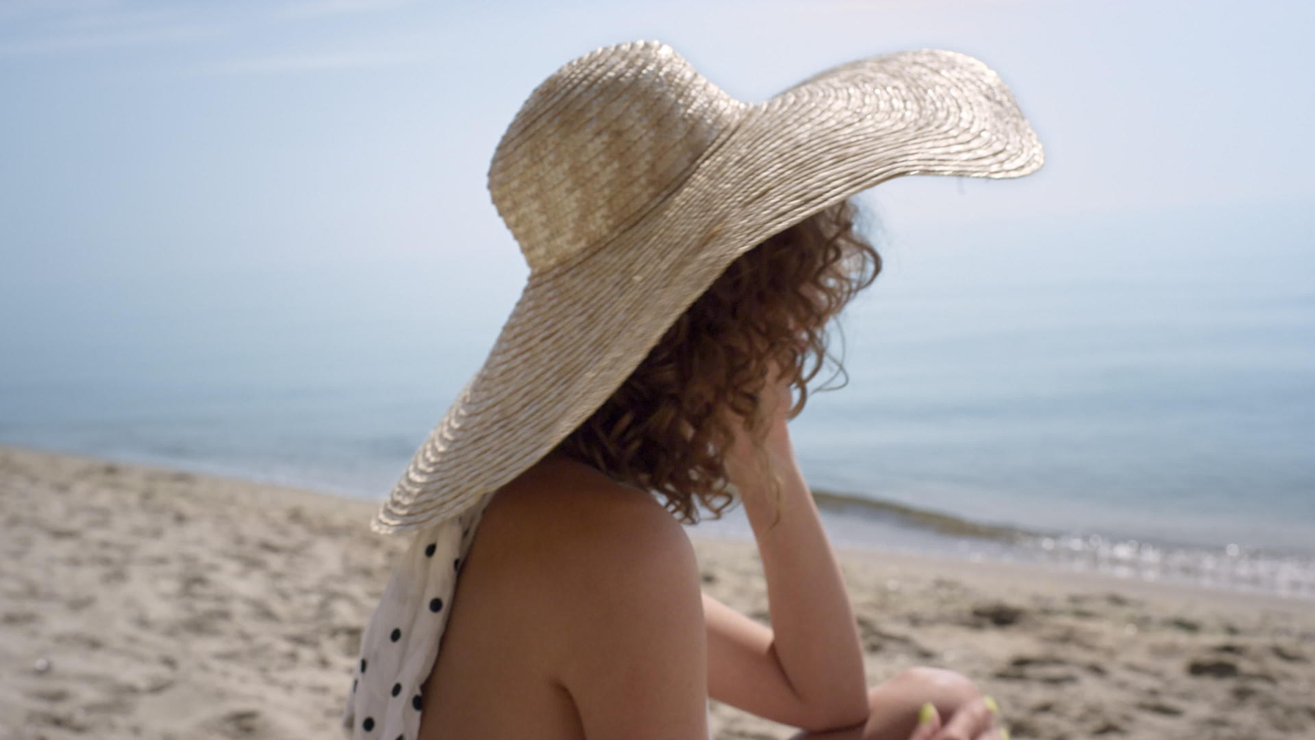 诱人的女人坐在沙滩上戴着宽边帽视频的预览图