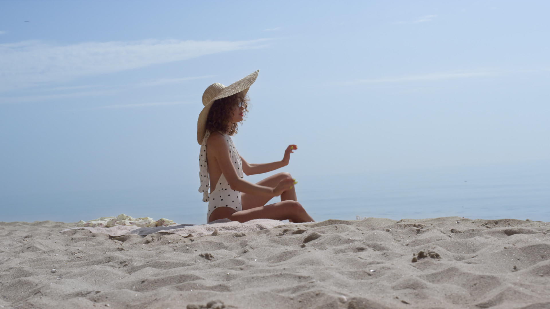 一位性感的女士戴着宽边帽坐在前面蓝天的沙子里视频的预览图