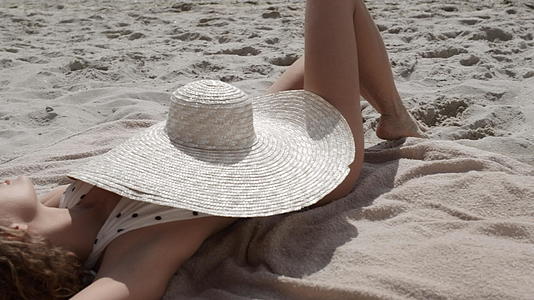遮住漂亮女人躺在沙滩上晒黑的身体宽边帽视频的预览图